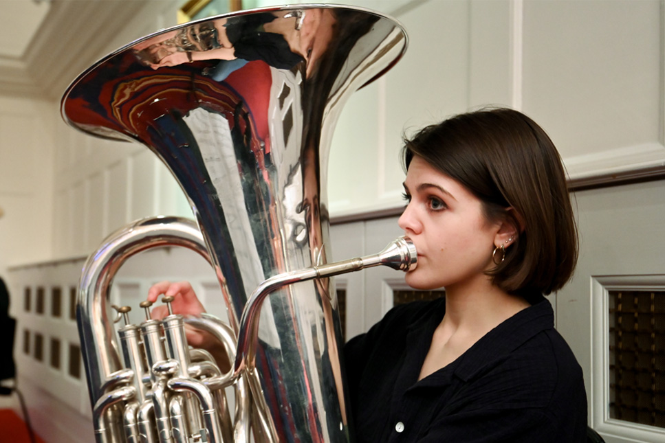 A female tuba player, wearing a black top, performing in a rehearsal.